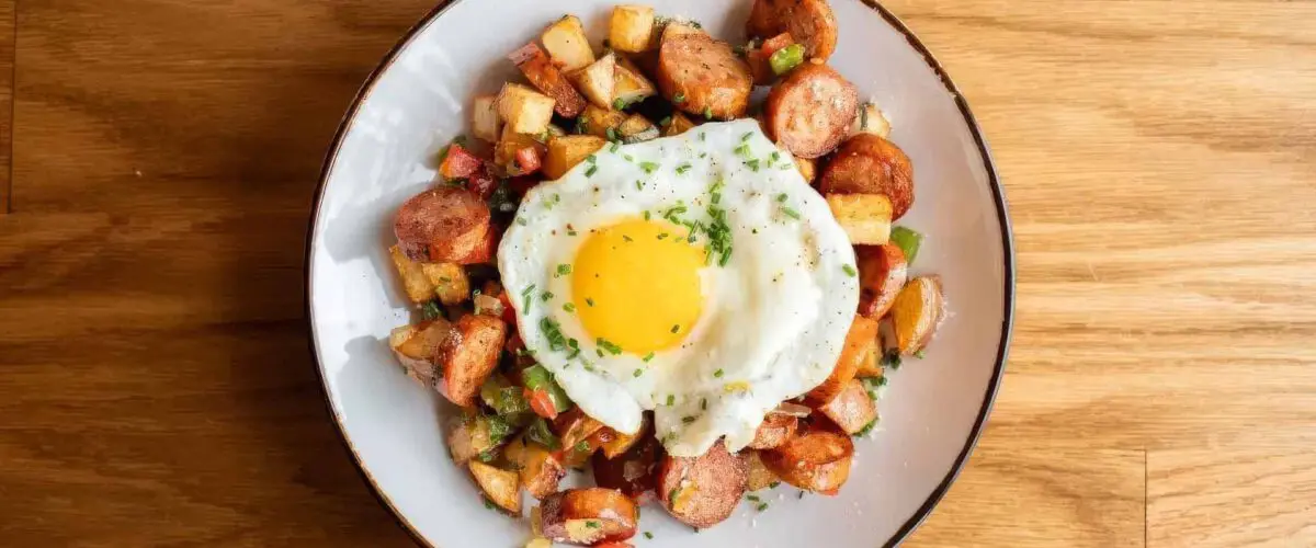 Overhead view of egg, sausage and potatoes in a white plate on a wood table