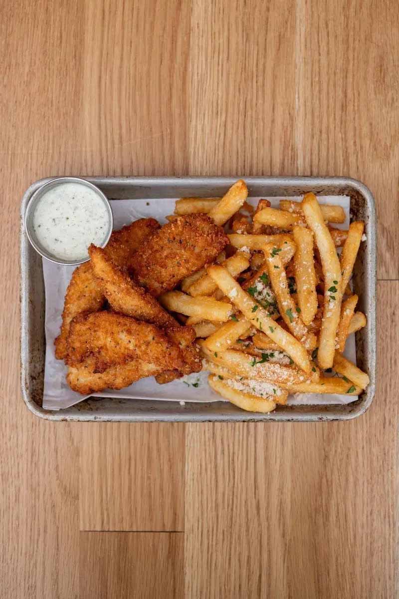 Overhead view of chicken tenders, fries and ranch on metal tray sitting on wooden table